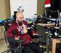 Man in a chair drinking from a cup held by a robotic arm